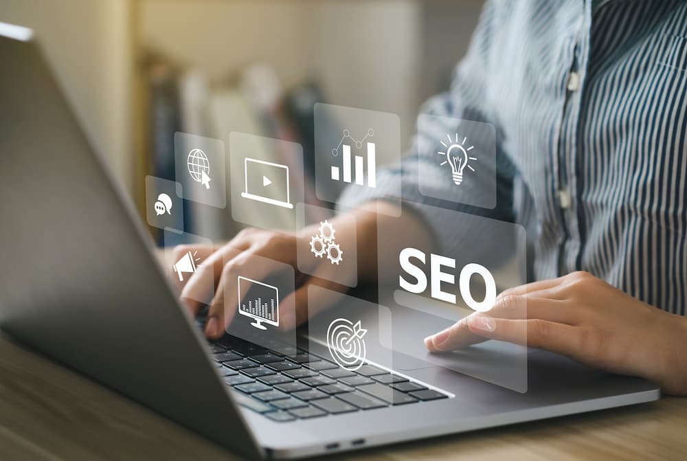 Person bedient Laptop mit SEO und Marketing Grafiken im Vordergrund