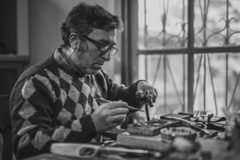 Handwerker sitzt an der Werkbank und arbeitet konzentriert an einem Werkstück mit Werkzeugen.
