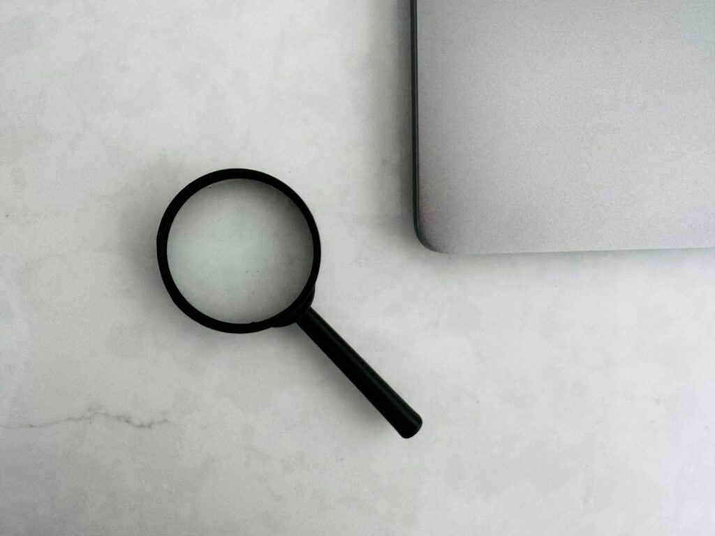 Lupe und Laptop auf Schreibtisch – Google Ads vs. SEO im Vergleich